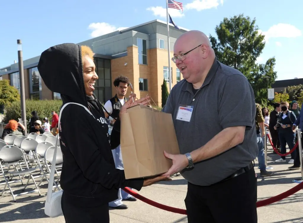 A man hands a young man a bag while both smile. 