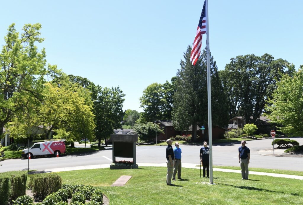 People standing by an American flag on a flag pole in a park. 