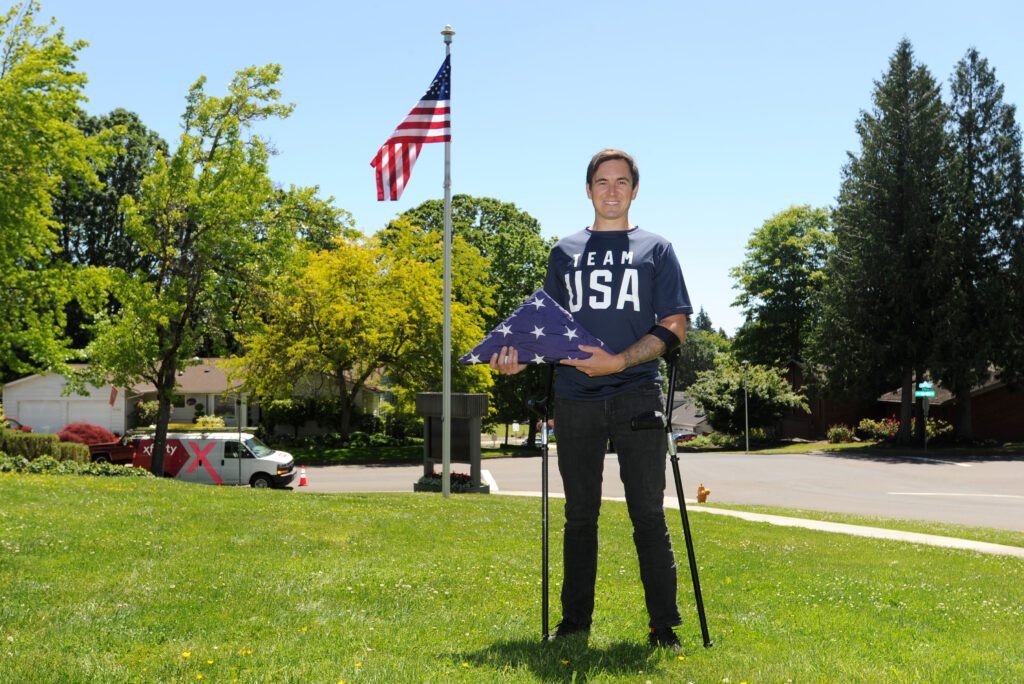 A man stands in front of a flag on a flag pole in a park. 